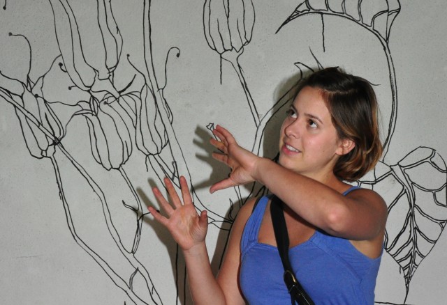 Eine Frau steht vor einem Kunstwerk und erklärt etwas.